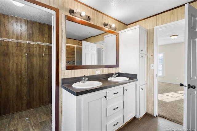 bathroom featuring hardwood / wood-style floors, vanity, ornamental molding, wooden walls, and a textured ceiling