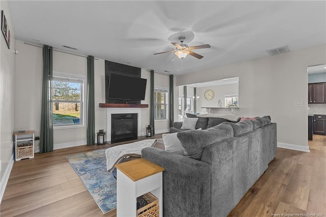 living room featuring ceiling fan, light hardwood / wood-style floors, and a fireplace