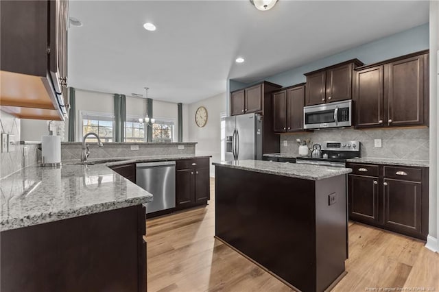 kitchen featuring appliances with stainless steel finishes, a center island, sink, light wood-type flooring, and light stone counters