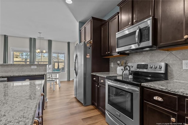 kitchen featuring light hardwood / wood-style floors, pendant lighting, dark brown cabinetry, appliances with stainless steel finishes, and light stone counters