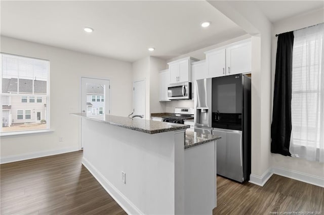 kitchen with appliances with stainless steel finishes, an island with sink, white cabinets, and dark stone counters