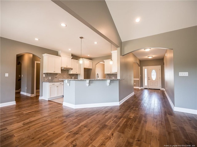 kitchen featuring dark wood-type flooring, vaulted ceiling, pendant lighting, tasteful backsplash, and white cabinetry