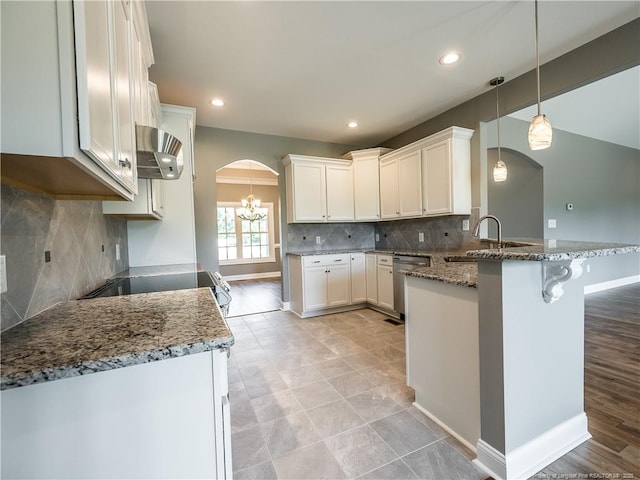 kitchen featuring sink, white cabinets, kitchen peninsula, stainless steel dishwasher, and dark stone counters