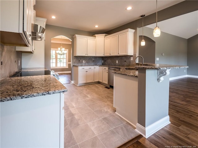 kitchen with dark stone countertops, dishwasher, kitchen peninsula, white cabinetry, and decorative light fixtures