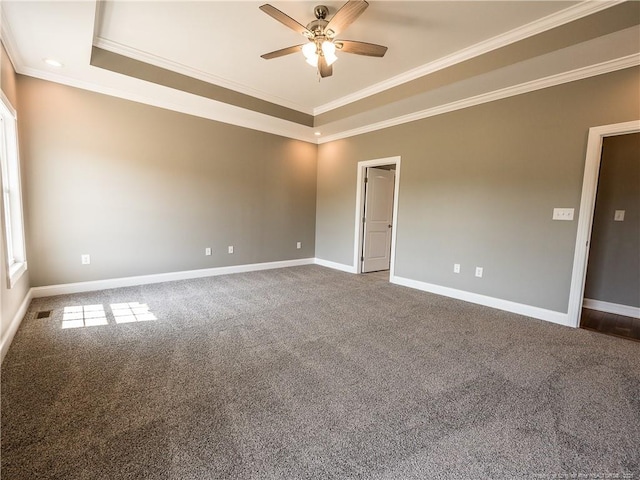 empty room featuring ornamental molding, dark colored carpet, and a tray ceiling