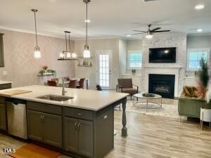 kitchen with sink, dishwasher, a large fireplace, an island with sink, and pendant lighting