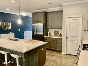 kitchen featuring a center island with sink, stainless steel fridge with ice dispenser, light wood-type flooring, hanging light fixtures, and sink