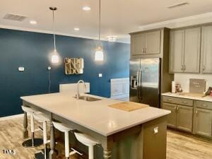 kitchen with light hardwood / wood-style floors, hanging light fixtures, an island with sink, stainless steel fridge, and sink