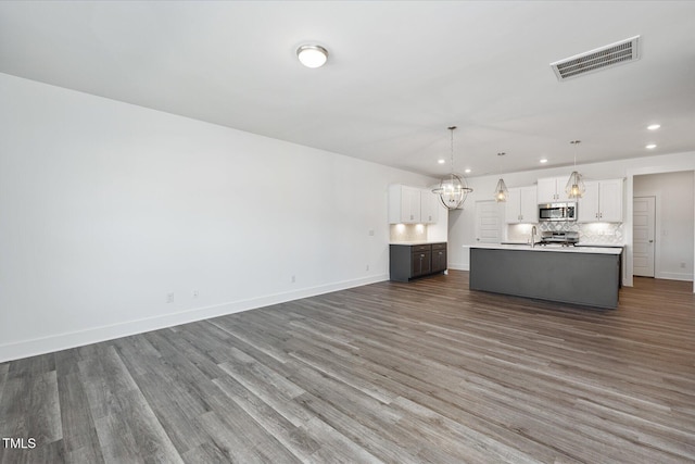 kitchen with an island with sink, appliances with stainless steel finishes, dark wood-type flooring, pendant lighting, and white cabinets