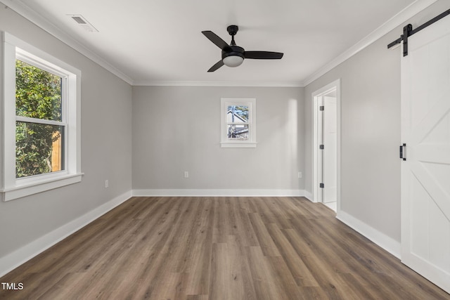 unfurnished room with ornamental molding, dark hardwood / wood-style floors, a barn door, and plenty of natural light