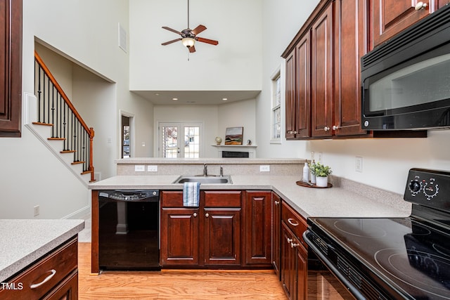 kitchen with black appliances, light hardwood / wood-style floors, a towering ceiling, ceiling fan, and sink