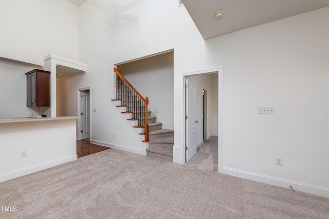 unfurnished living room with a high ceiling, ceiling fan, and dark colored carpet