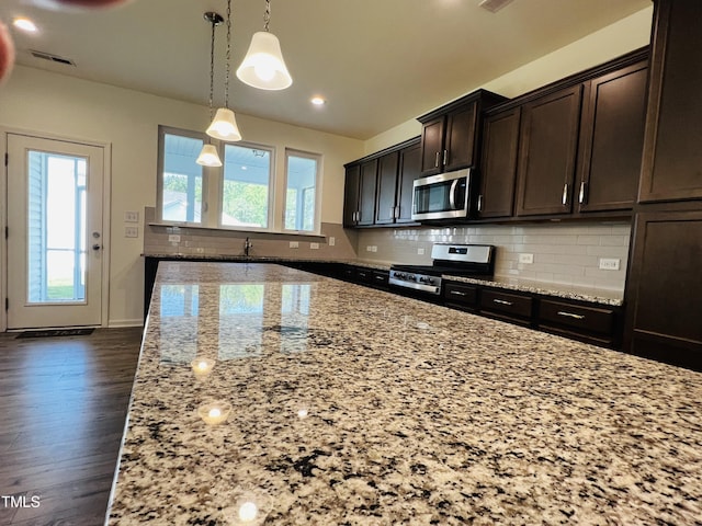 kitchen with dark brown cabinetry, hanging light fixtures, stainless steel appliances, light stone countertops, and decorative backsplash