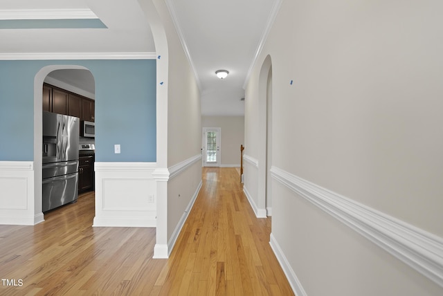 hall with crown molding, light wood-style flooring, a decorative wall, and arched walkways