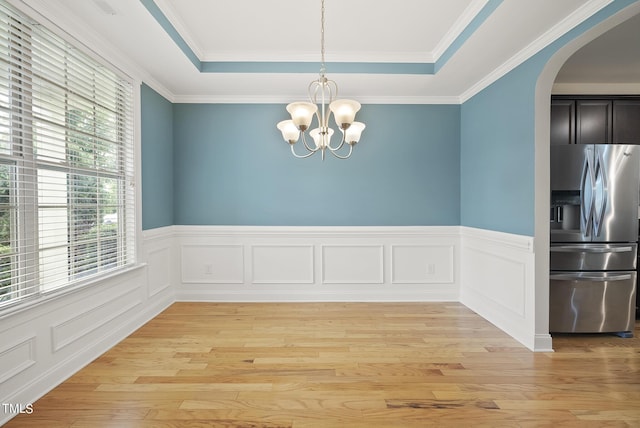 unfurnished dining area with a chandelier, arched walkways, a raised ceiling, and light wood-style floors