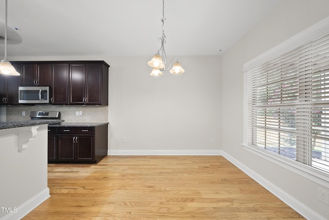 kitchen with light wood-type flooring, pendant lighting, stainless steel microwave, backsplash, and dark brown cabinets