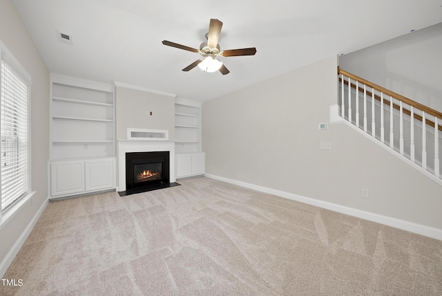 unfurnished living room with stairway, visible vents, baseboards, a fireplace with flush hearth, and light carpet