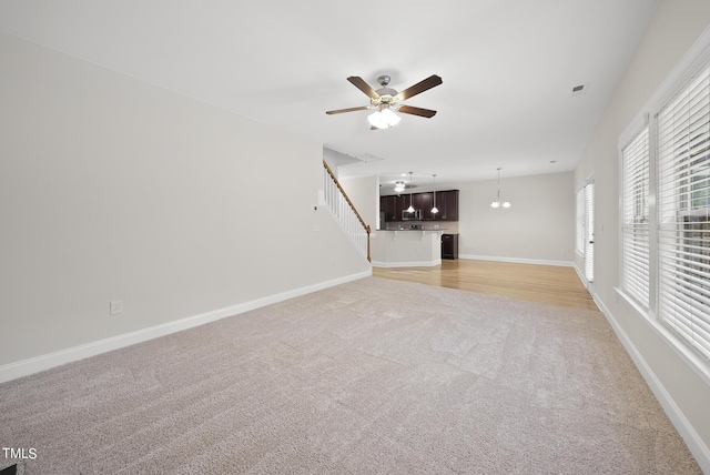 unfurnished living room with light colored carpet, a ceiling fan, and baseboards