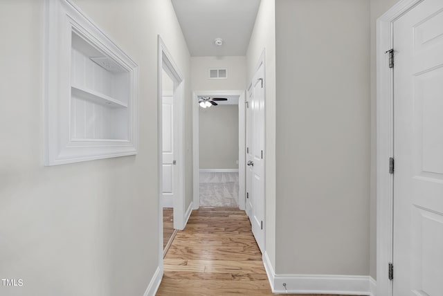 hall featuring light wood-style flooring, baseboards, and visible vents