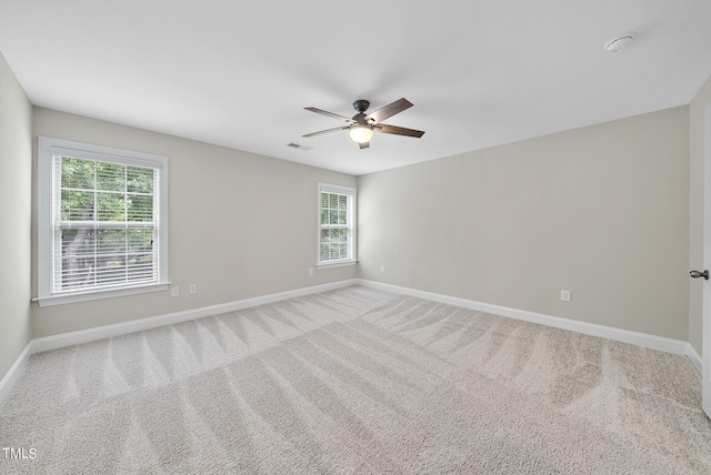 carpeted spare room with visible vents, baseboards, and ceiling fan