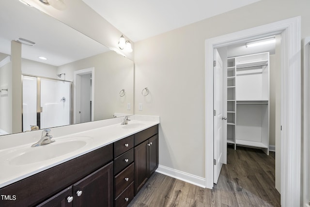 full bathroom with a spacious closet, a stall shower, wood finished floors, and a sink