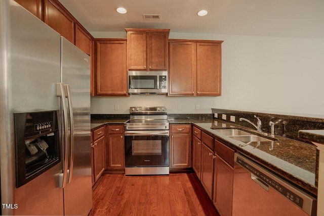 kitchen featuring appliances with stainless steel finishes, dark stone counters, sink, and hardwood / wood-style flooring