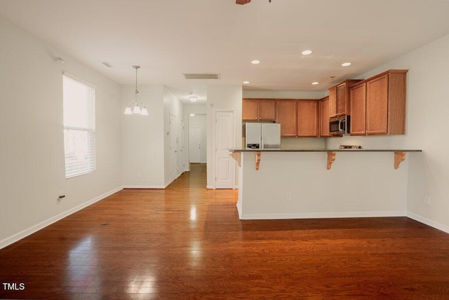 kitchen featuring appliances with stainless steel finishes, an inviting chandelier, hanging light fixtures, a breakfast bar, and dark wood-type flooring