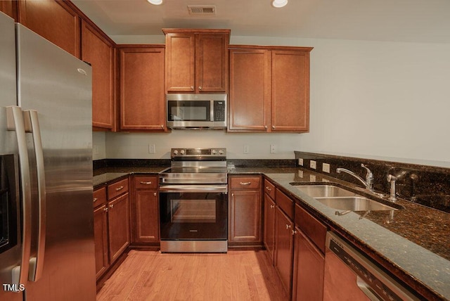 kitchen with appliances with stainless steel finishes, light hardwood / wood-style floors, dark stone counters, and sink