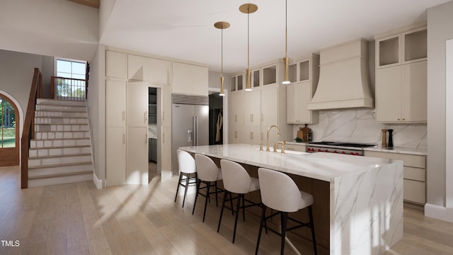 kitchen featuring light stone countertops, pendant lighting, custom exhaust hood, sink, and a center island with sink