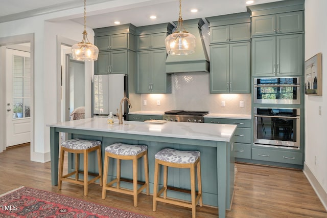 kitchen with custom exhaust hood, white fridge, a center island with sink, pendant lighting, and green cabinetry