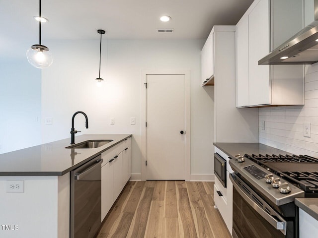 kitchen featuring sink, white cabinetry, wall chimney exhaust hood, pendant lighting, and appliances with stainless steel finishes