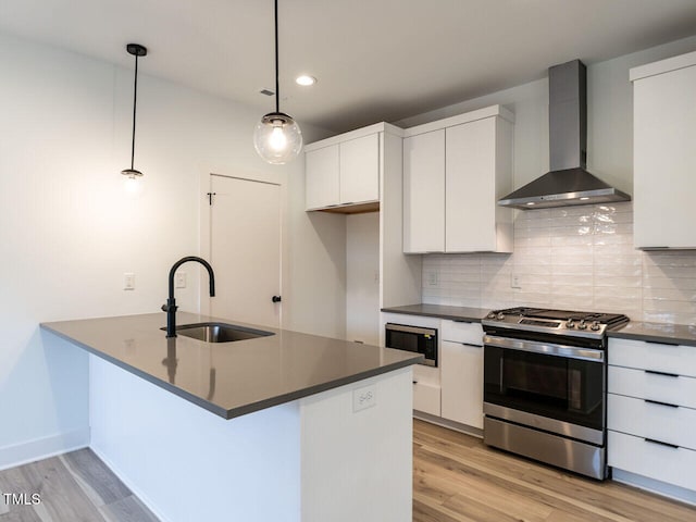 kitchen featuring sink, decorative light fixtures, white cabinetry, wall chimney range hood, and appliances with stainless steel finishes