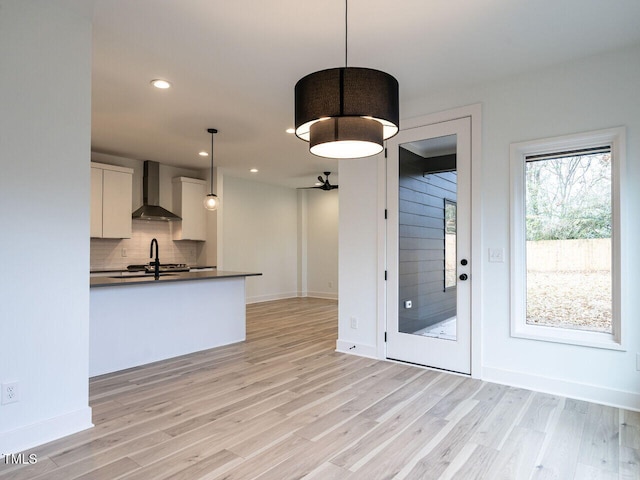 kitchen featuring decorative light fixtures, white cabinets, wall chimney exhaust hood, and light hardwood / wood-style flooring