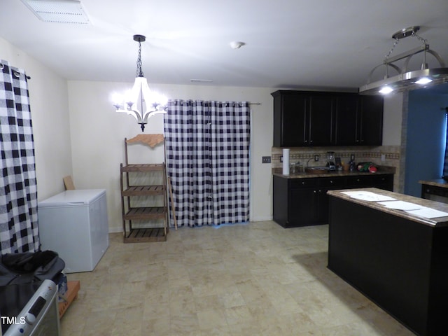 kitchen featuring tasteful backsplash, visible vents, dark cabinets, refrigerator, and a notable chandelier