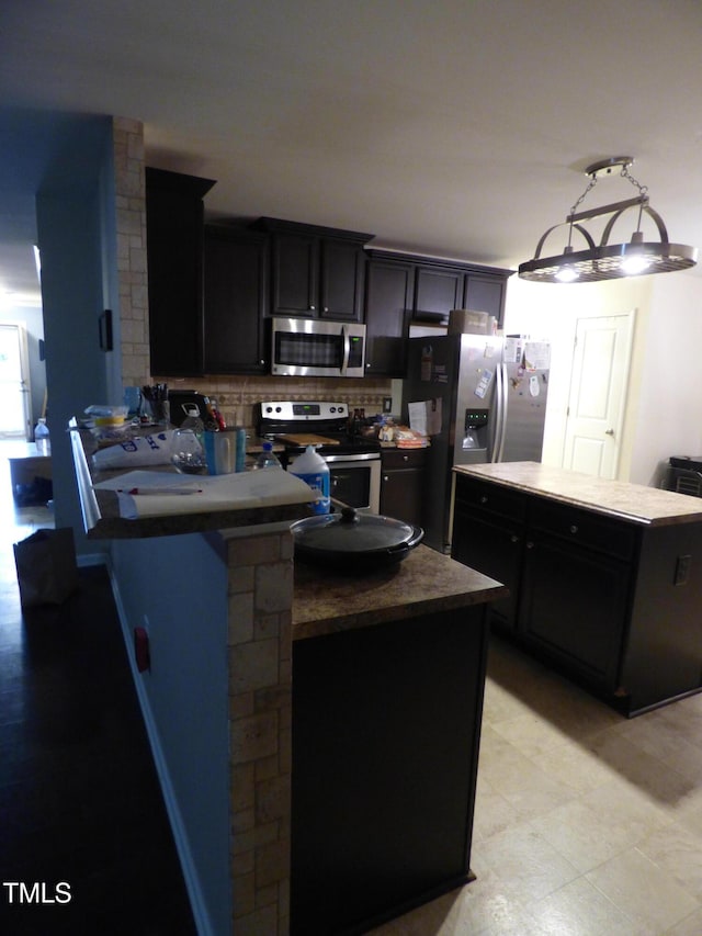 kitchen featuring tasteful backsplash, dark countertops, a kitchen island, appliances with stainless steel finishes, and dark cabinetry