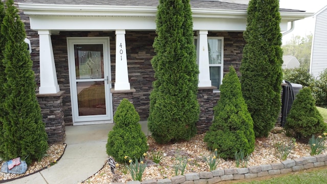 view of exterior entry featuring a porch, a shingled roof, and stone siding