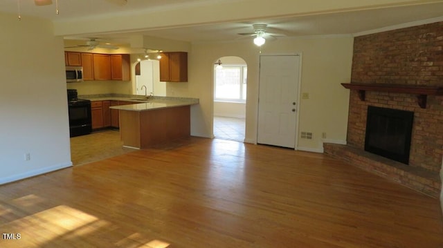 kitchen with kitchen peninsula, light hardwood / wood-style flooring, black / electric stove, a brick fireplace, and sink