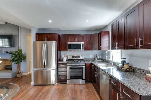 kitchen featuring wood-type flooring, appliances with stainless steel finishes, sink, and dark stone countertops