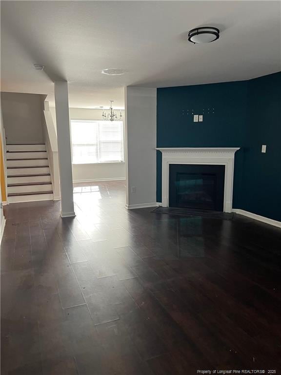 unfurnished living room with baseboards, a glass covered fireplace, an inviting chandelier, and stairway