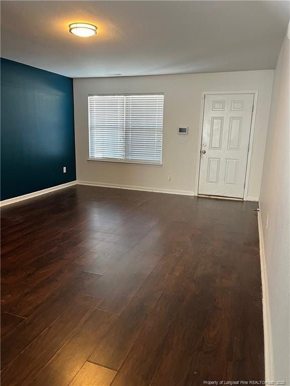 empty room featuring dark wood-type flooring and baseboards