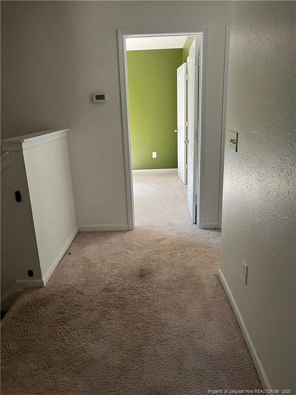 hall featuring baseboards and light colored carpet