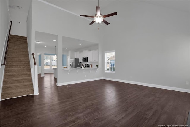 unfurnished living room with ceiling fan, dark hardwood / wood-style flooring, plenty of natural light, and a high ceiling