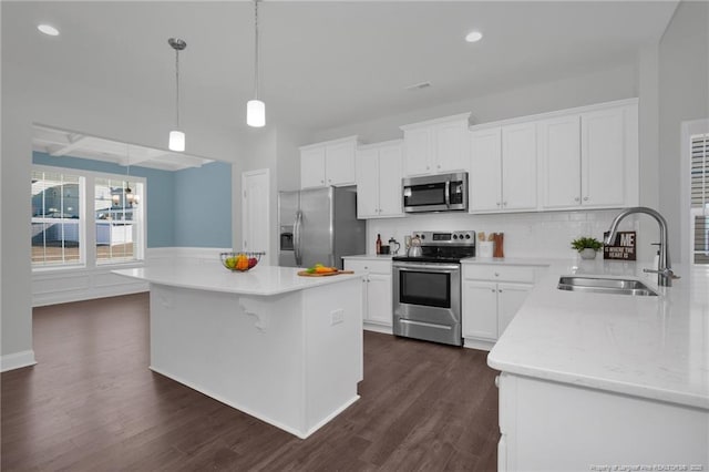 kitchen featuring stainless steel appliances, hanging light fixtures, a kitchen island, sink, and white cabinetry