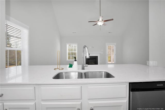 kitchen featuring white cabinets, vaulted ceiling, light stone counters, sink, and stainless steel dishwasher