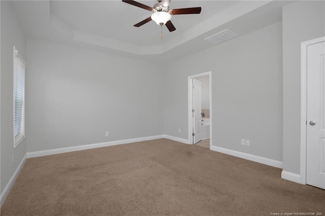 spare room with ceiling fan, a tray ceiling, and light colored carpet