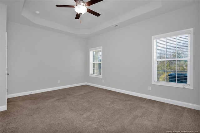 carpeted empty room featuring ceiling fan, plenty of natural light, and a tray ceiling