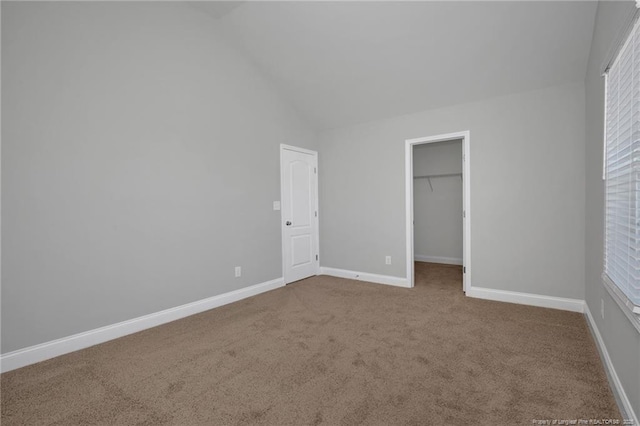 unfurnished bedroom with lofted ceiling, a closet, a spacious closet, and carpet flooring