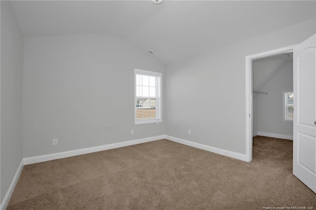 unfurnished bedroom featuring lofted ceiling, a walk in closet, a closet, and carpet