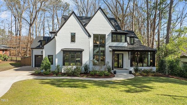 view of front of house featuring driveway, metal roof, a standing seam roof, a front yard, and brick siding