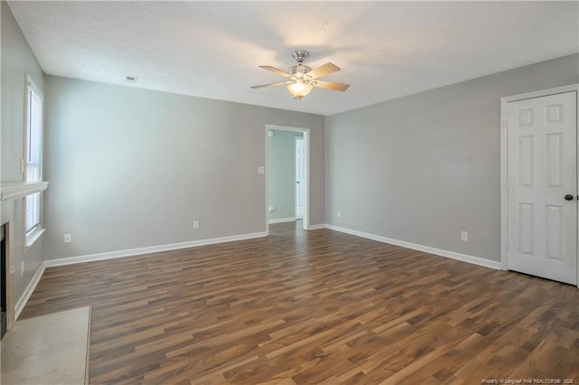 unfurnished living room featuring ceiling fan, a premium fireplace, and dark wood-type flooring